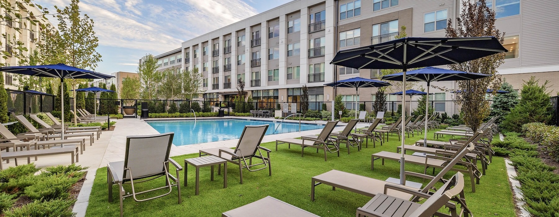 The pool area at Sagewell Hanover Apartments For Rent in Hanover, MA, featuring lounge chairs and umbrellas.